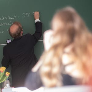 Ein Lehrer schreibt etwas an die Tafel.