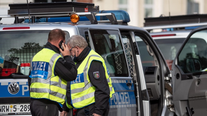 Ein Polizist steht telefonierend an einem Tatort, sein Kollege geht mit Spurensicherungskoffer zum Einsatzwagen.