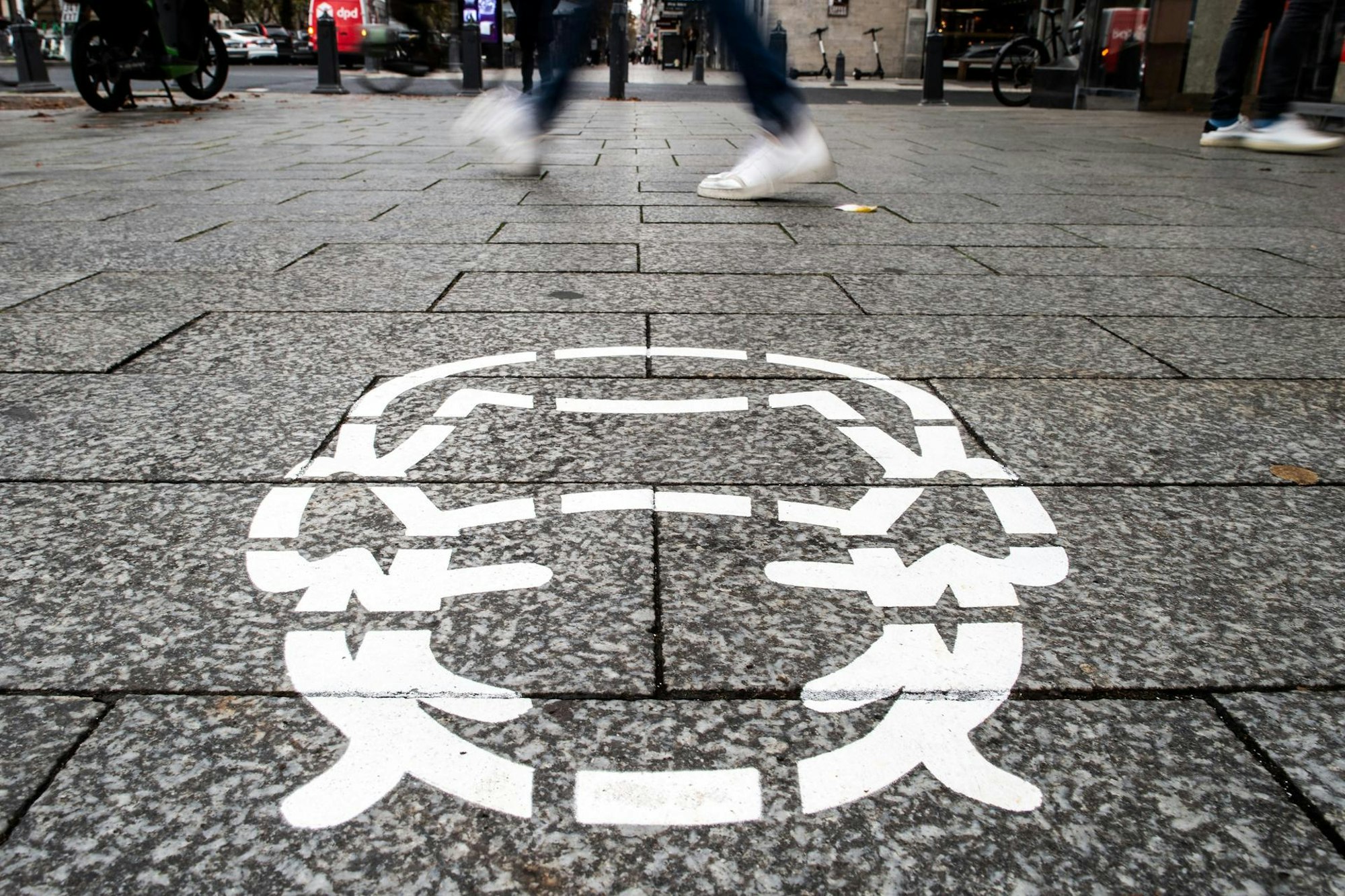 Corona-Piktogramme wurden als Hinweis auf die Maskenpflicht auf einem Bürgersteig in Düsseldorf gesprüht.