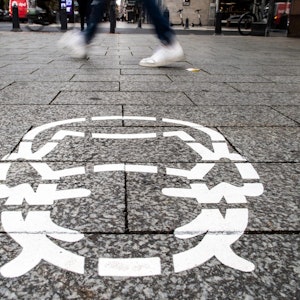 Corona-Piktogramme wurden als Hinweis auf die Maskenpflicht auf einem Bürgersteig in Düsseldorf gesprüht.