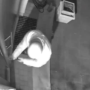 Ein hell gekleideter Einbrecher mit Mütze macht sich an einer Haustür zu schaffen.