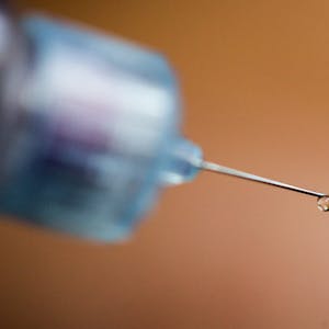 Ein Tropfen Insulin an der Nadel einer Spritze.