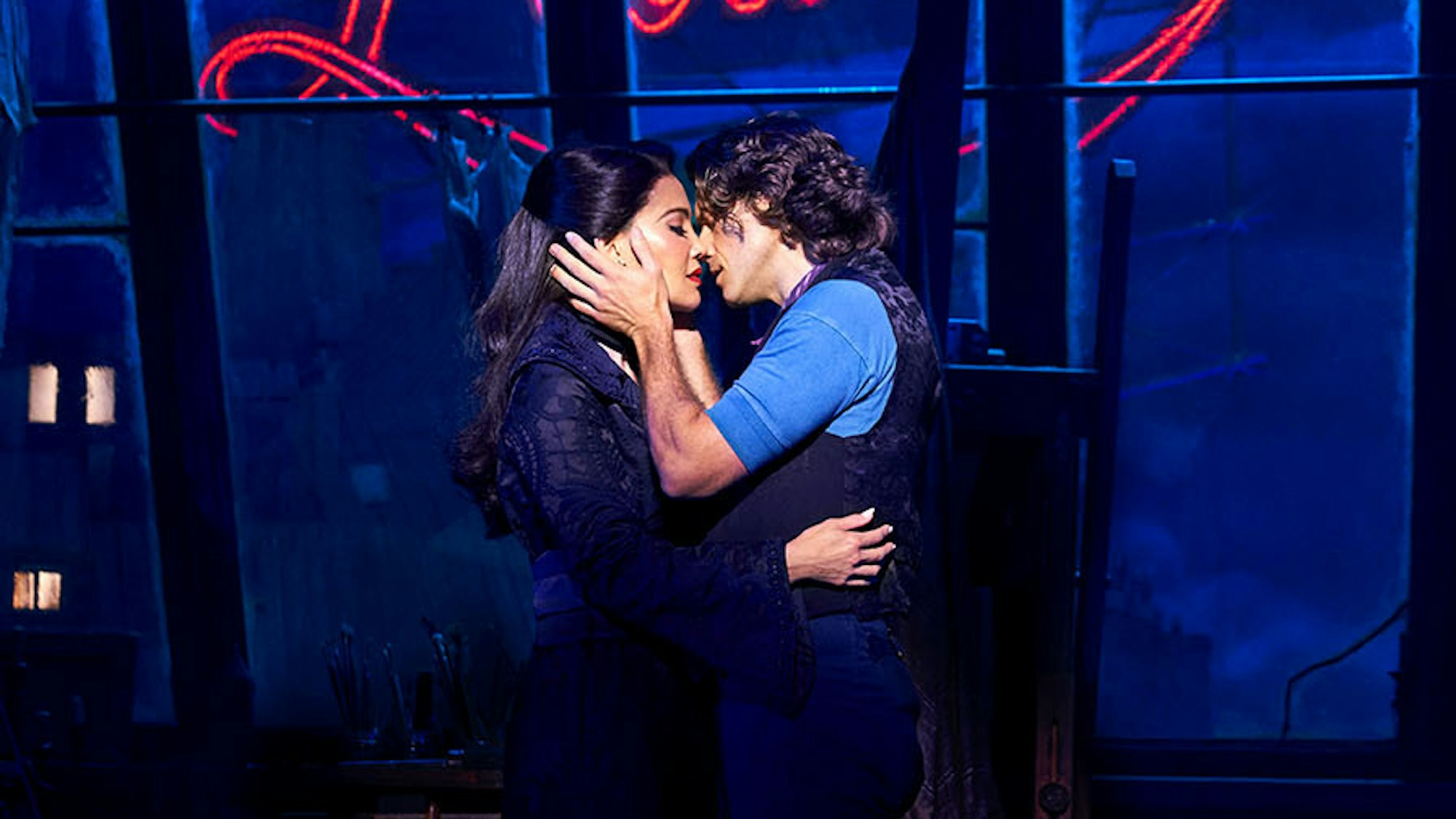 Die beiden Hauptdarsteller von Moulin Rouge küssen sich vor dem abendlichen Hintergrund mit Mühle und rotem Licht.