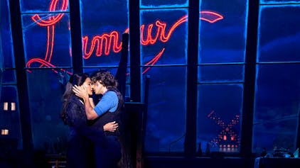 Die beiden Hauptdarsteller von Moulin Rouge küssen sich vor dem abendlichen Hintergrund mit Mühle und rotem Licht.