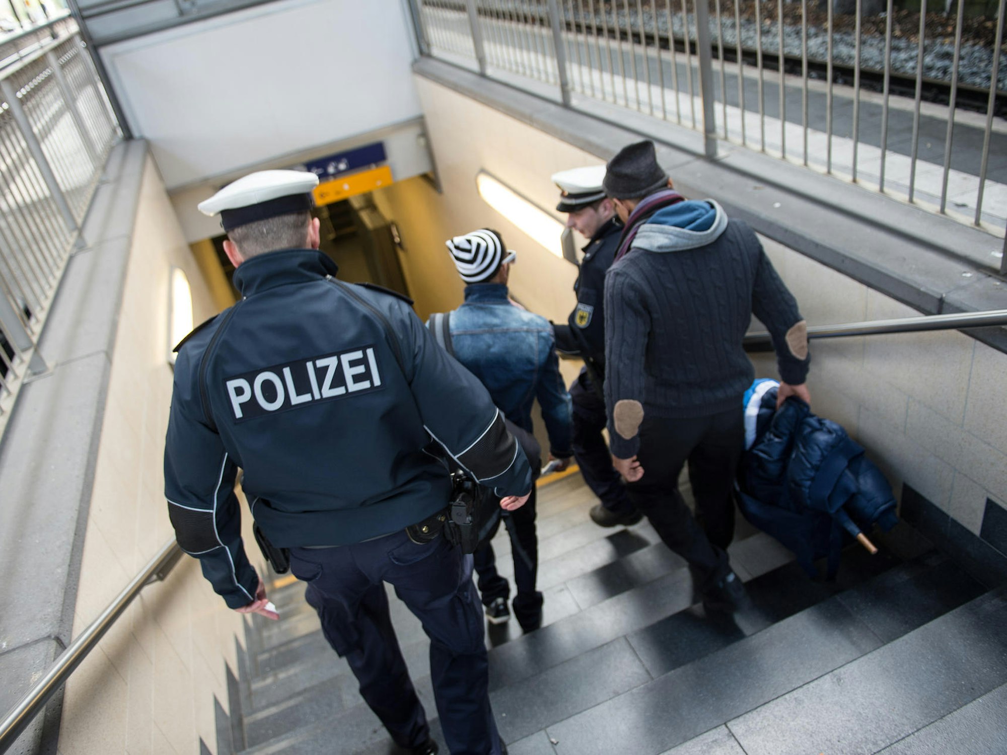 Zwei Polizisten gehen gemeinsam mit zwei Männern eine Treppe im Kölner Hauptbahnhof runter.