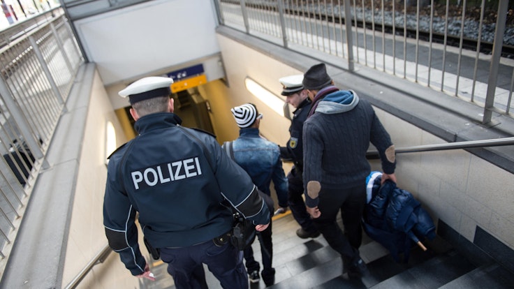 Zwei Polizisten gehen gemeinsam mit zwei Männern eine Treppe im Kölner Hauptbahnhof runter.