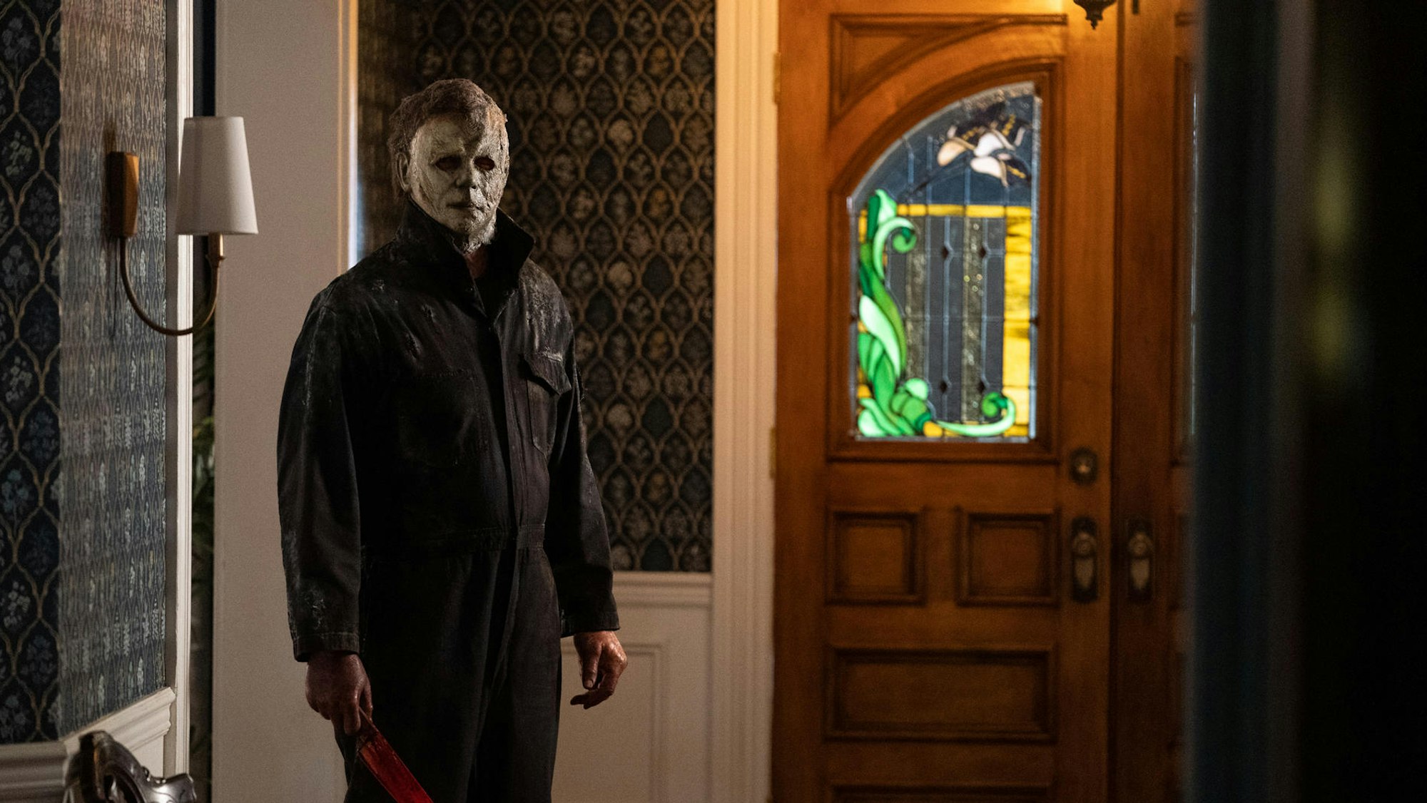 Die Hauptfigur der Halloween-Serie mit einem blutverschmiertem Messer steht im Flur eines Hauses. Er trägt seine berühmte, weiße Maske.