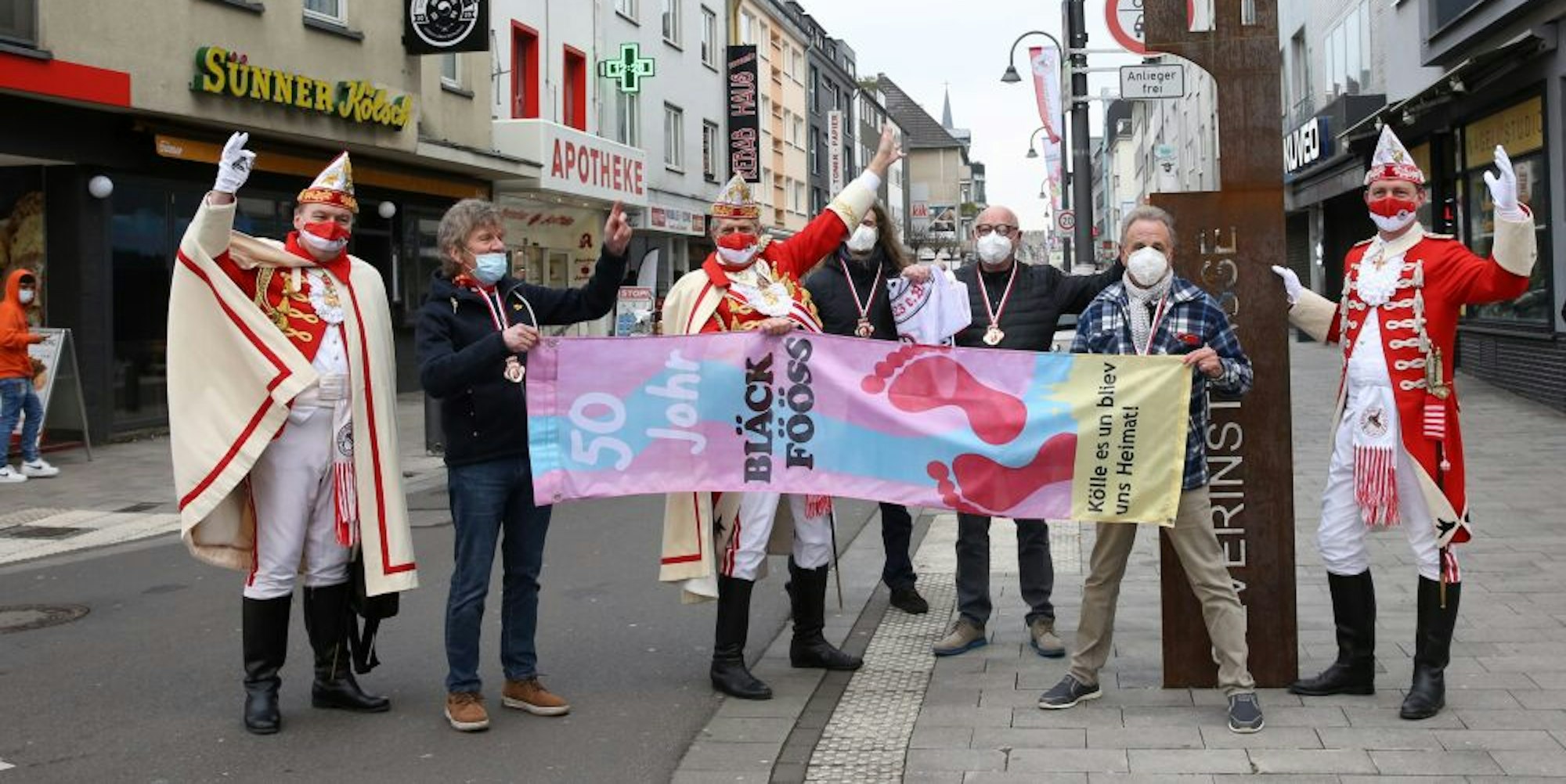Drei Rote Funken in großer Uniform und vier Mitglieder der Bläck Fööss auf der karnevalistisch beflaggten Severinstraße