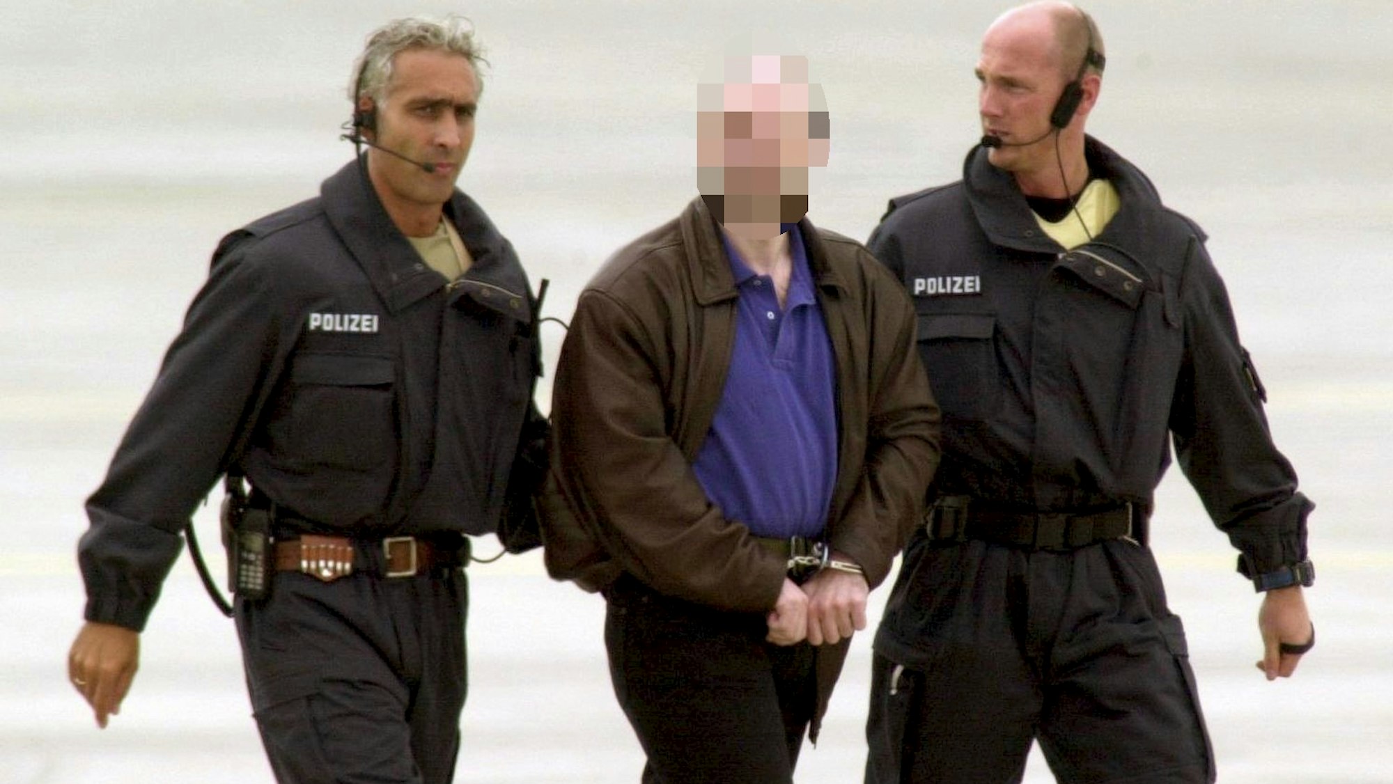 Zwei Polizisten begleiten Thomas Drach, der mit Handschellen gefesselt ist.