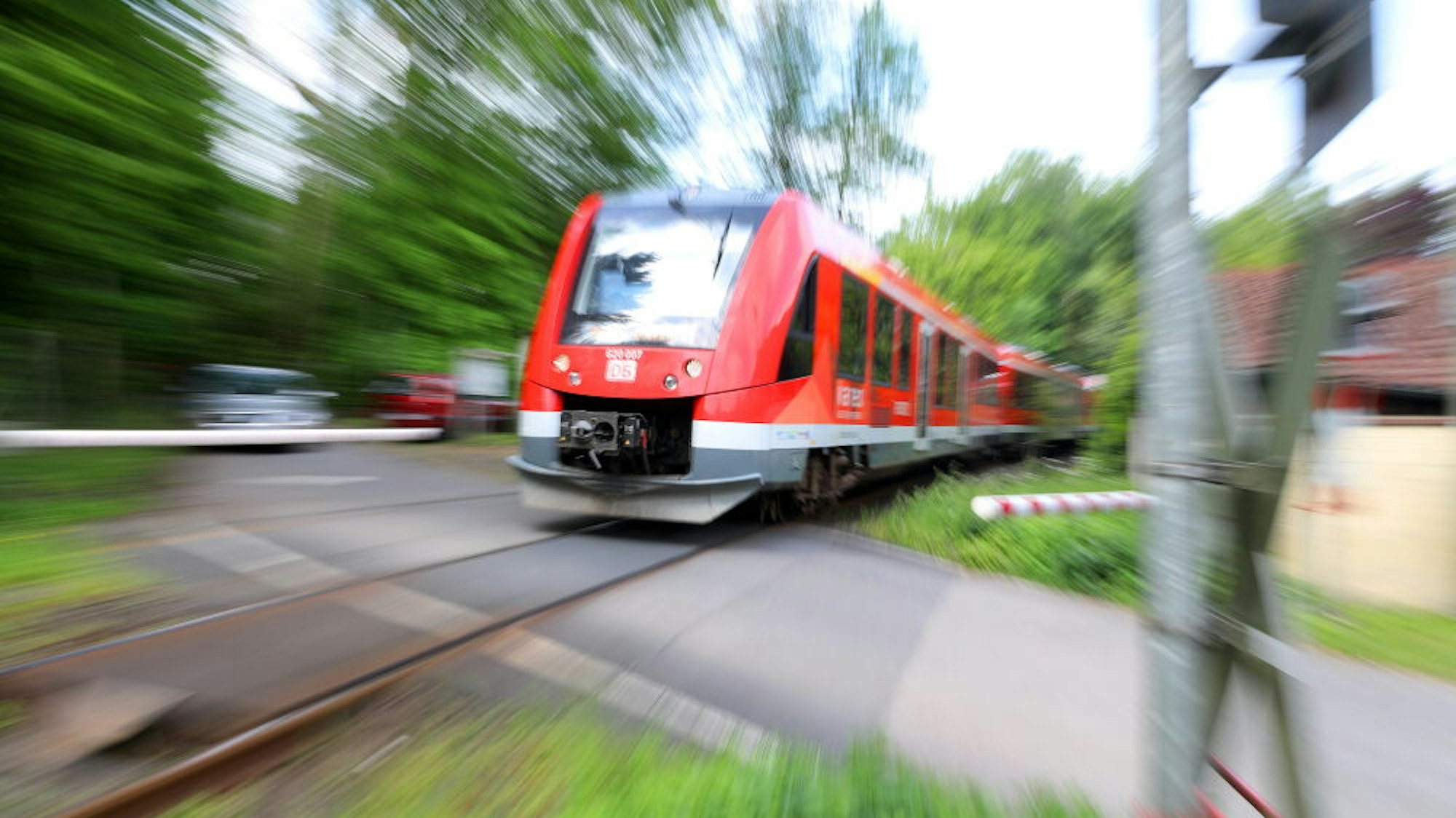 Ein Zug der Oberbergischen Bahn (Köln – Overath – Gummersbach) passiert einen beschrankten Bahnübergang.