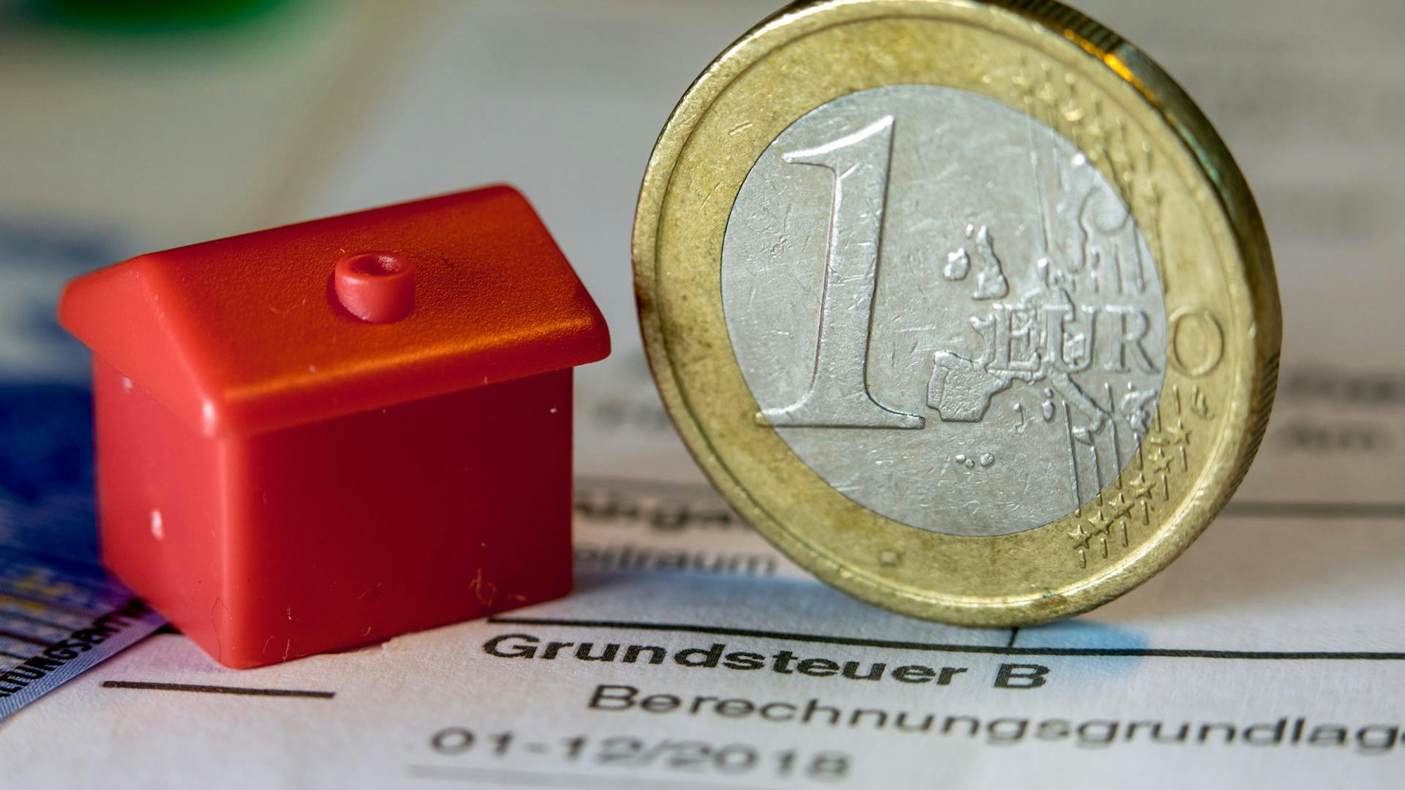 Eine 1€-Münze und ein Monopoly-Haus liegen auf einem Steuerbescheid.