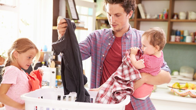 Ein Vater macht die Wäsche mit einem Baby auf dem Arm.