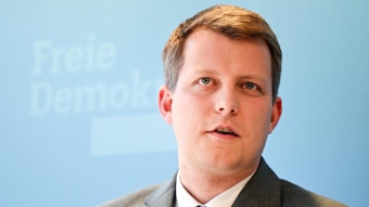 Henning Höne spricht bei einer Veranstaltung. Er ist im Porträt zu sehen vor einer hellblauen FDP-Werbewand.
