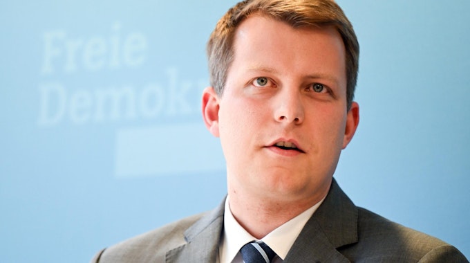 Henning Höne spricht bei einer Veranstaltung. Er ist im Porträt zu sehen vor einer hellblauen FDP-Werbewand.