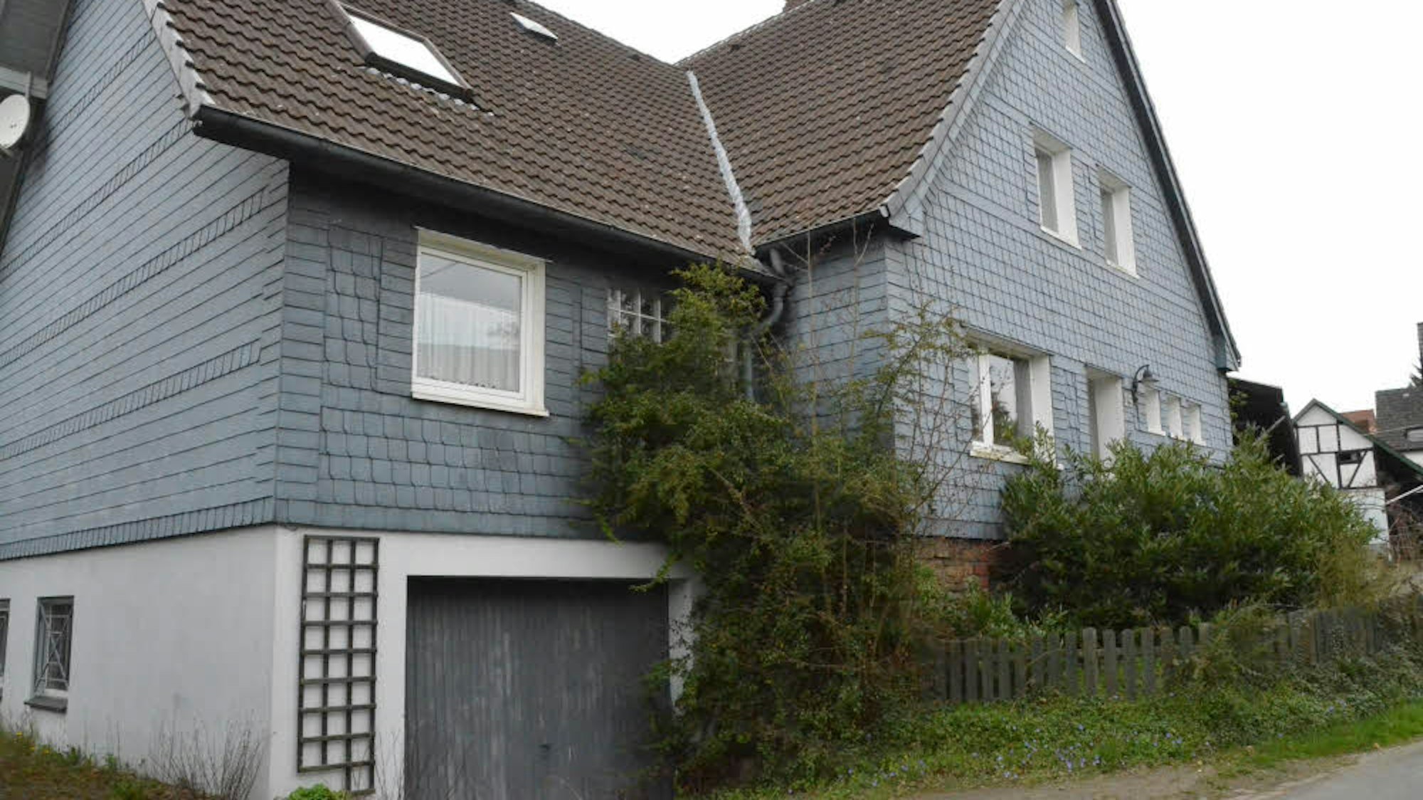 In der Morsbacher Ortschaft Steimelhagen steht ein großes Haus, dessen Großteil mit Schieferplatten verkleidet ist. Der Vorgarten ist zugewachsen.