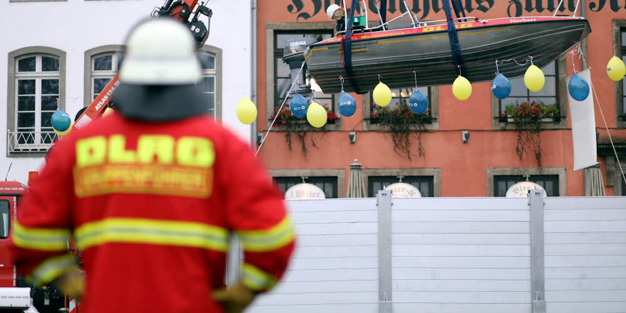 Ein Boot mit einer Puppe „schwimmt“ auf dem angenommenen Extremhochwasser in der Kölner Innenstadt, dessen Pegel die blauen und gelben Luftballons symbolisieren. Die graue Hochwasserschutzwand zeigt, bis zu welcher Höhe die Altstadt bisher geschützt ist.