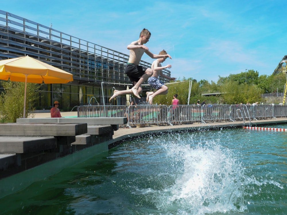 Kinder springen von einem Sprungbrett in ein Schwimmbecken.