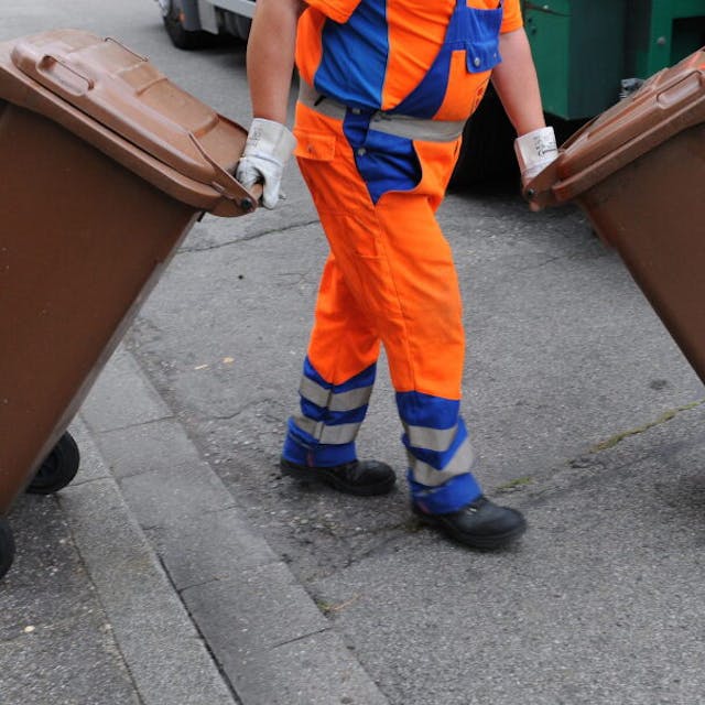 Das Foto zeigt einen Müllmann mit zwei braunen Tonnen