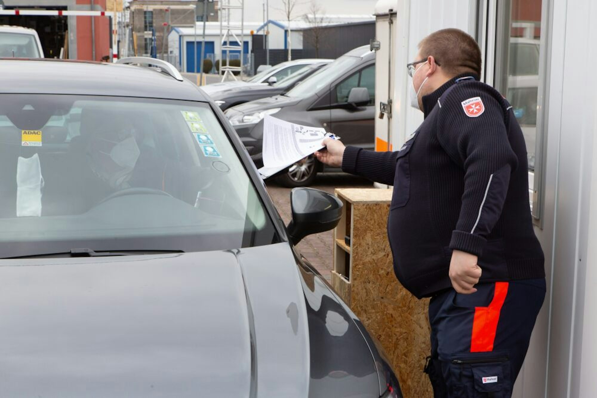 Die Unterlagen zum Test werden aus sicherer Entfernung ins Auto gereicht. Hier von einem Malteser Helfer.