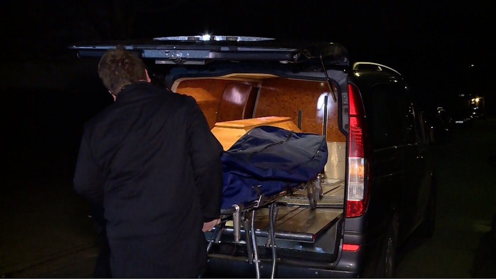 Ein Bestatter schiebt einen Leichnam in den Leichenwagen.