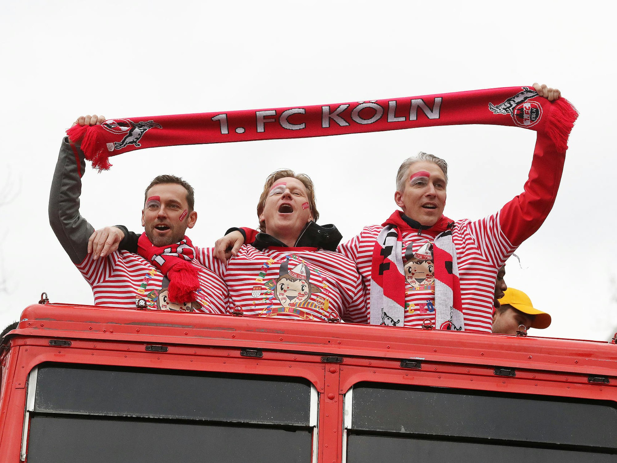 Drei Männer halten einen Schal des 1. FC Köln auf einem Karnevalswagen.