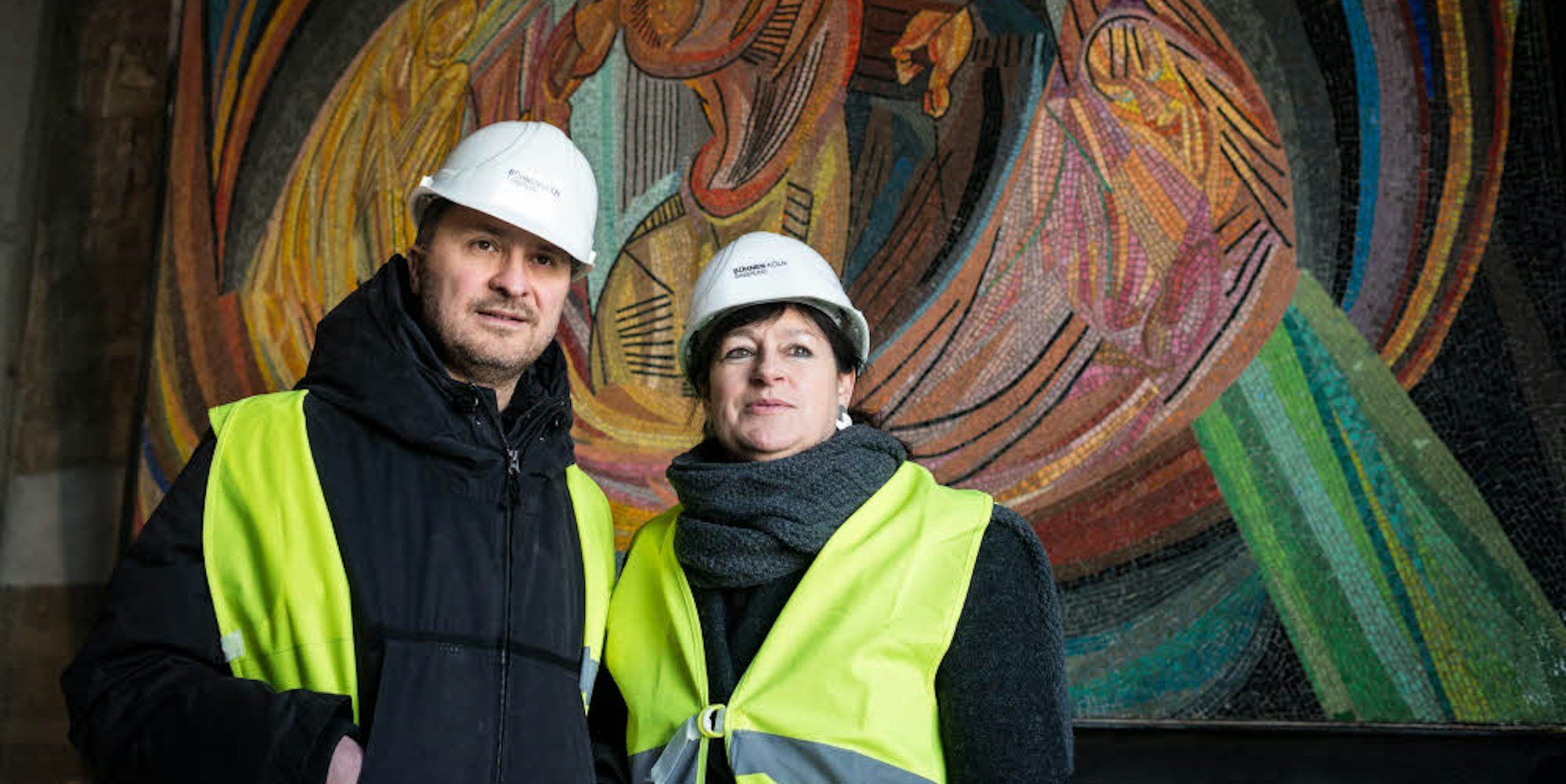 Kulturschaffende in Arbeitermontur: Yilmaz Dziewior, Direktor des Museums Ludwig, und Opernintendantin Birgit Meyer stehen auf der Opernbaustelle vor dem Mosaik von Otto Freundlich.