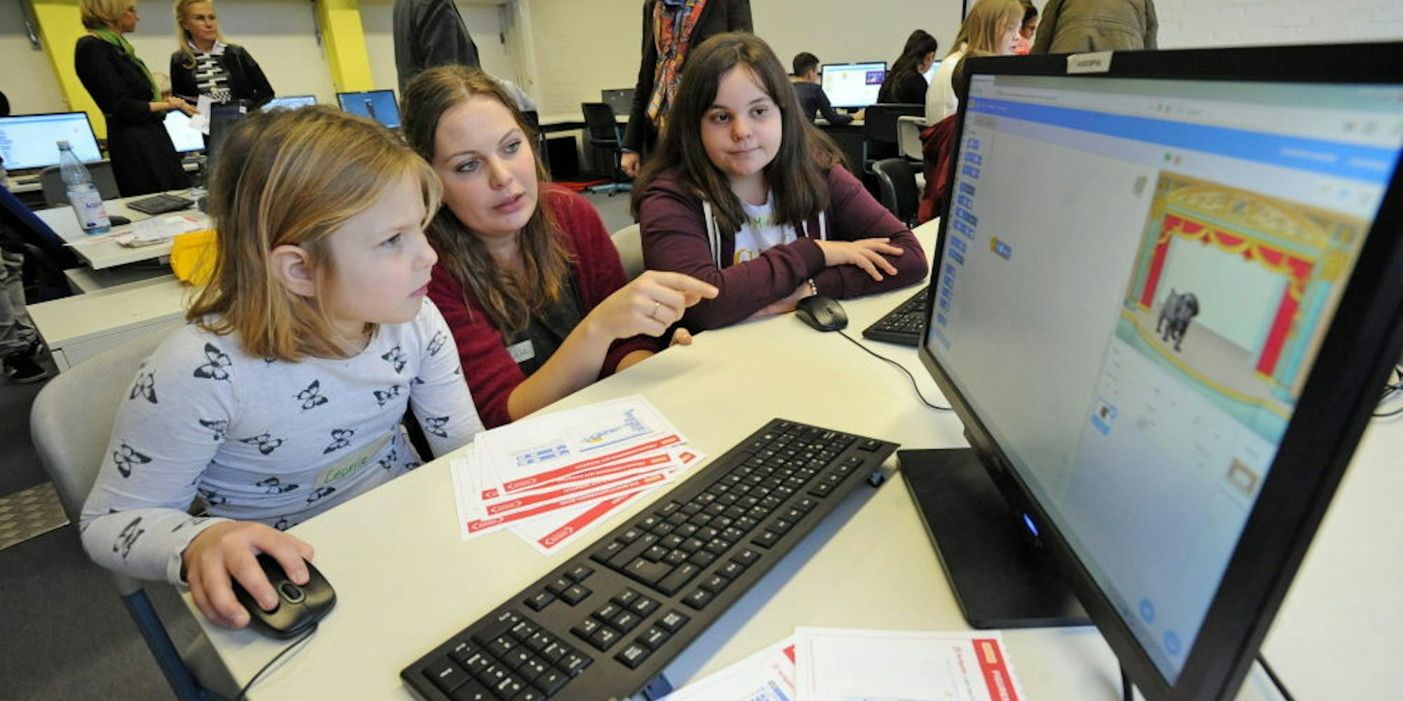 Projektmitarbeiterin Lisa Mütsch (M) hilft Leonie (l) und Mia beim Programmieren.