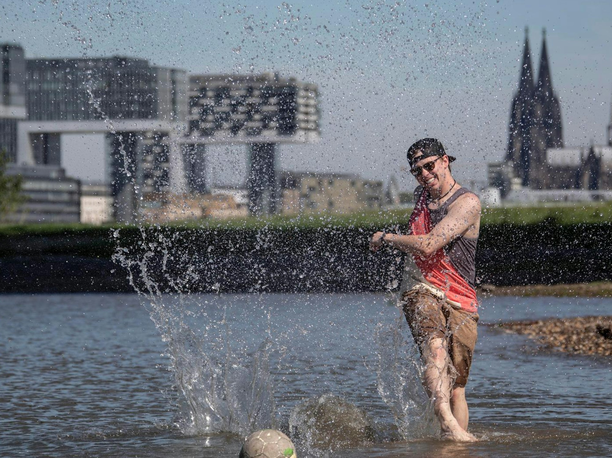 Junger Mann spielt bei Hitze Fußball im Rhein Köln.