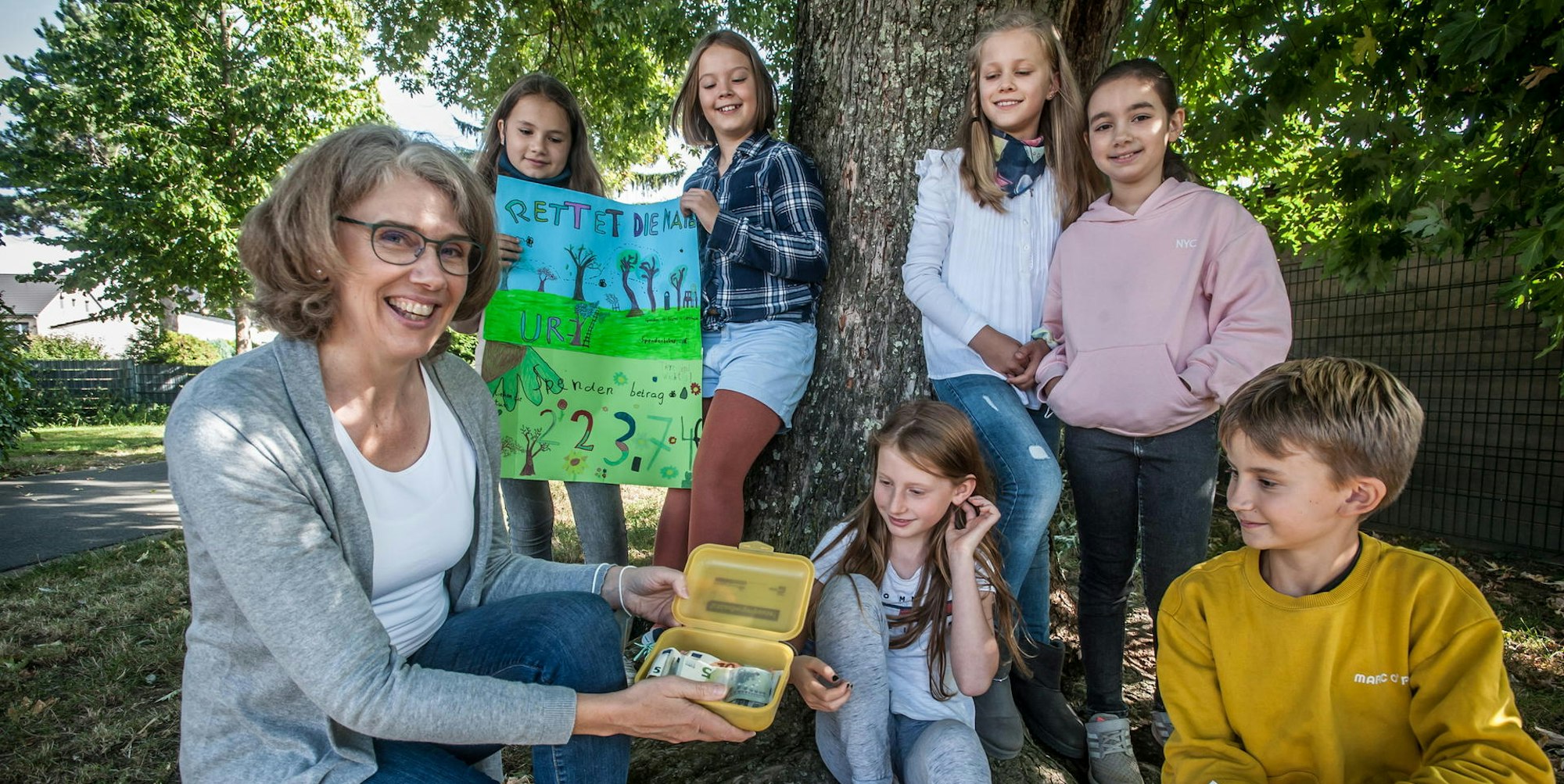 Die Drittklässlerin Emilia übergibt gemeinsam mit fünf Mitschülern die gesammelten Spenden an Sabine Strippel, Vereinsgründerin von „Bäume für Leverkusen“.