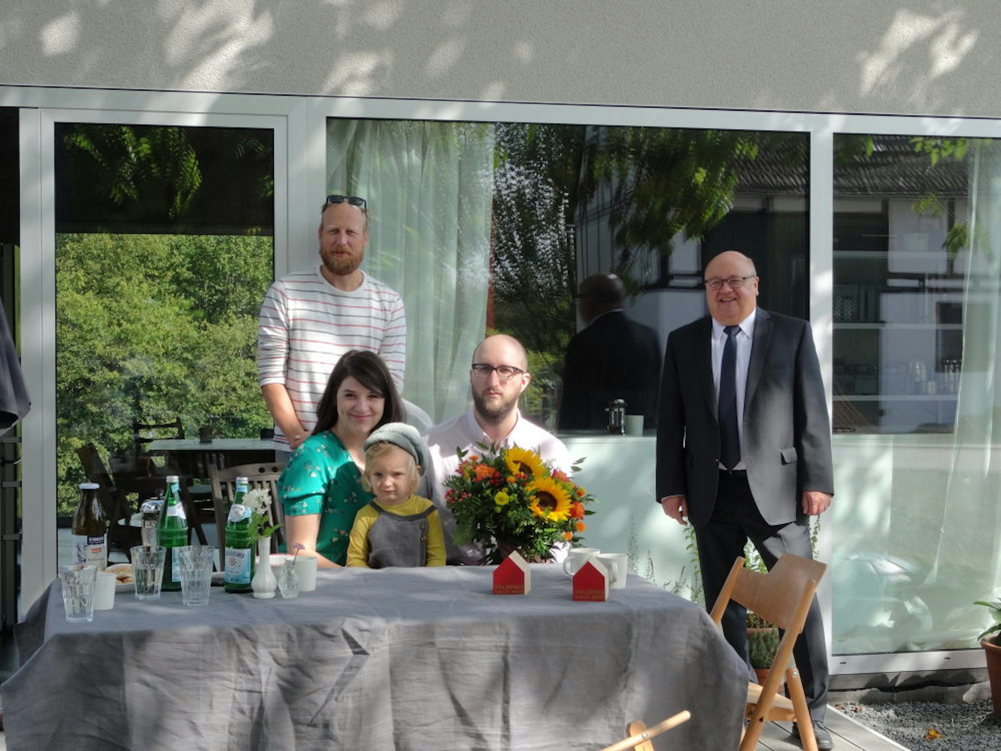 Sara und Benjamin Bell (am Tisch mit dem zweijährigen Friedrich) haben sich ihr Haus vom Architekten Wolfgang Zeh (hinten links) bauen lassen. Das Ehepaar gewann einen Sonderpreis, den Frank Rethwisch, Bezirksleiter der LBS Lohmar, überreichte.