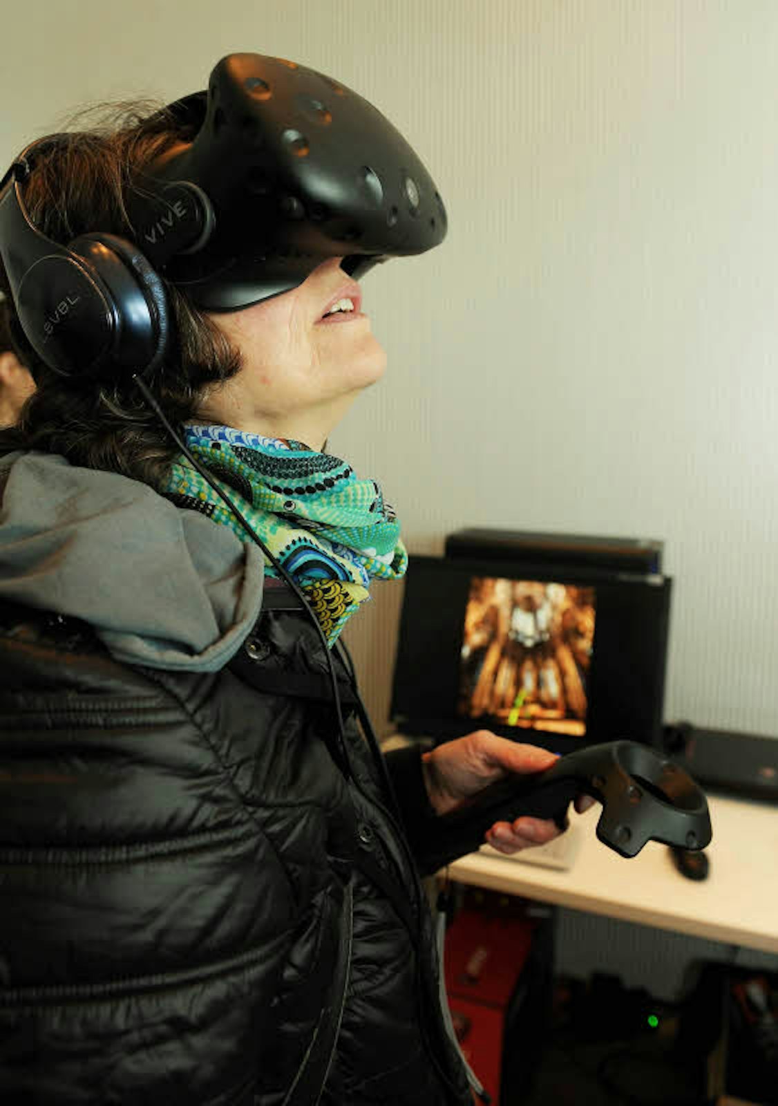 Mit der VR-Brille lässt sich das Bild, das auf dem Bildschirm im Hintergrund zu sehen ist, in 3D virtuell und interaktiv erkunden. Mit dem Joystick steuert man den Rundgang.