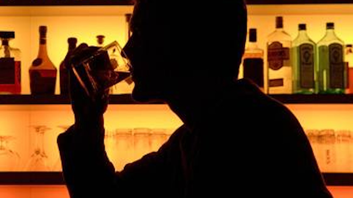 Eine Person sitzt an einer Bar und trinkt an einem Glas.