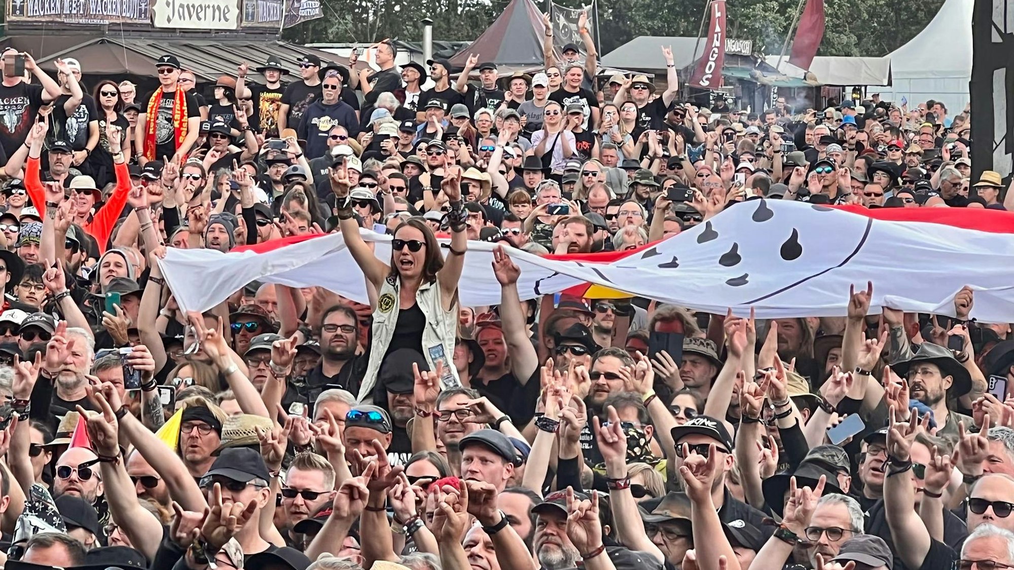 Fans jubeln in Wacken und zeigen eine große Fahne mit dem Kölner Stadtwappen.