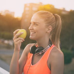 Eine Frau in Sportkleidung hält einen Apfel in der Hand.&nbsp;
