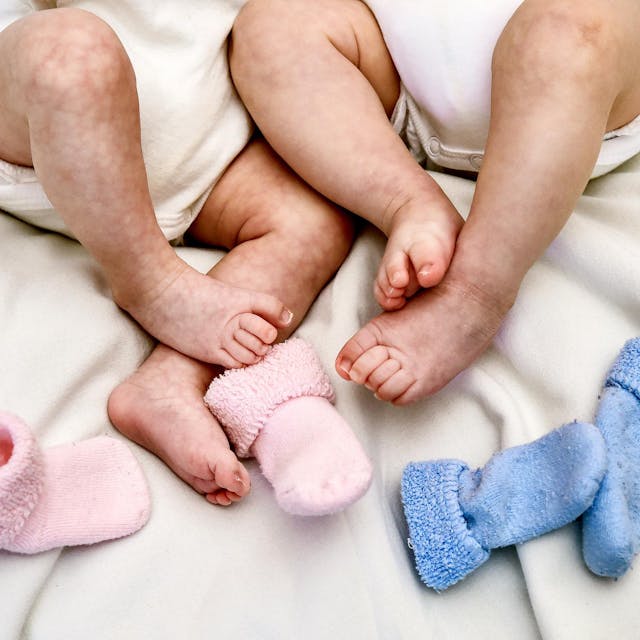 Zwei Babys liegen im Bett und zeigen ihre Füße.