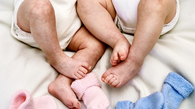 Zwei Babys liegen im Bett und zeigen ihre Füße.