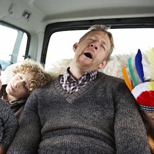 Müder Vater sitzt mit drei Kindern im Auto.