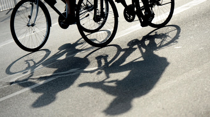 Die Schatten zweier Radfahrer auf einer Straße.