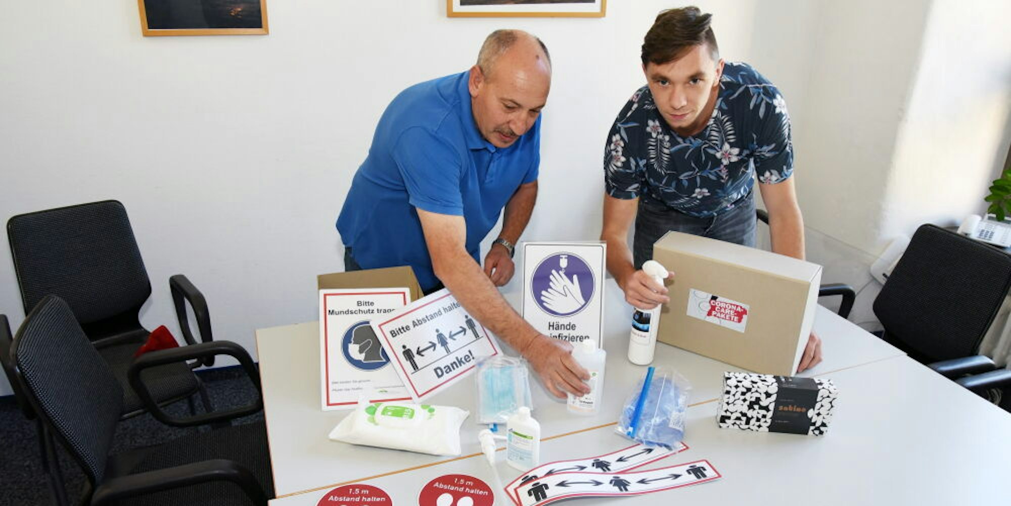 Jedes Wahllokal in der Gemeinde Engelskirchen bekommt ein „Corona-Care-Paket“. Hausmeister Salvatore Fiandaca (l.) und Azubi Marvin Schnabel zeigen, was sich darin befindet.
