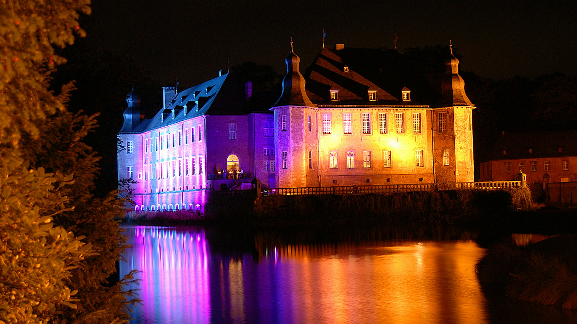 Das historische Wasserschloss ist lila und rot angeleuchtet.