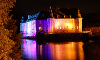 Das historische Wasserschloss ist lila und rot angeleuchtet.