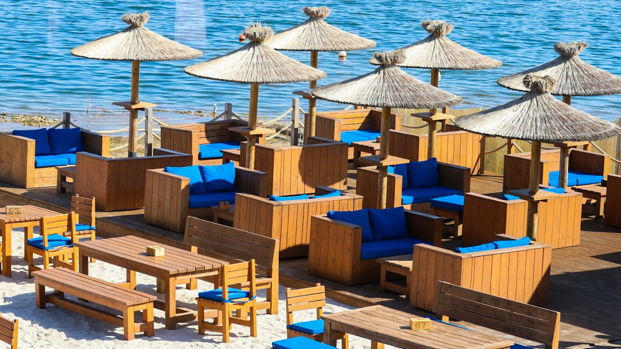 Holztische und Stühle mit Strohsonnenschirmen am Strand