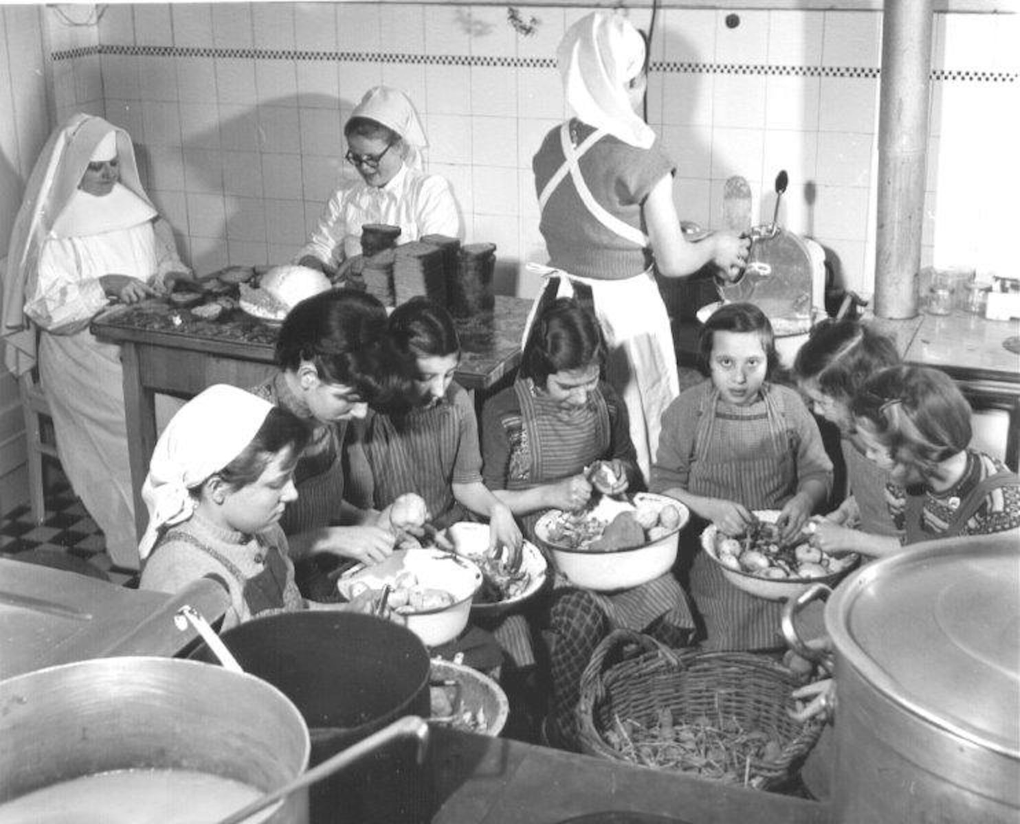 Eine Küchenschwester, eine Lernschwester, eine Küchenhelferin und eine Mädchengruppe bereiten das Essen im Kreiskinderheim in Brauweiler vor, das von 1950 bis 1958 bestand.