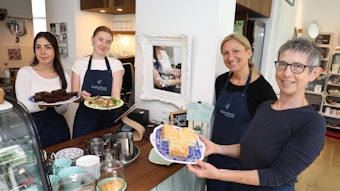 Vier Mitarbeiterinnen des neuen Cafés in Overath stehen am Tresen und halten Teller mit Gerichten in der Hand.