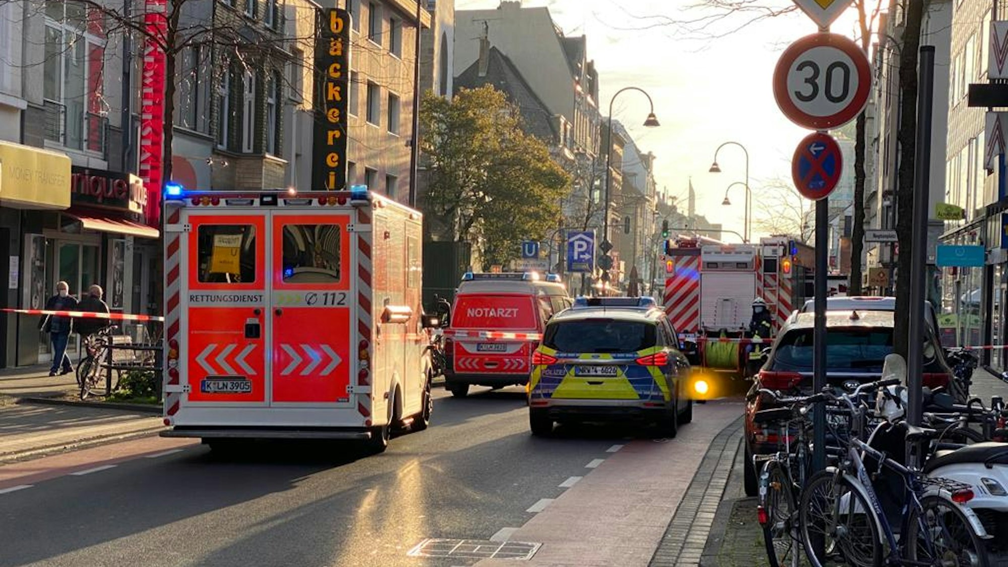 Die Venloer Straße ist mit Flatterband abgesperrt, Fahrzeuge von Polizei, Rettungsdienst und Feuerwehr stehen dort.