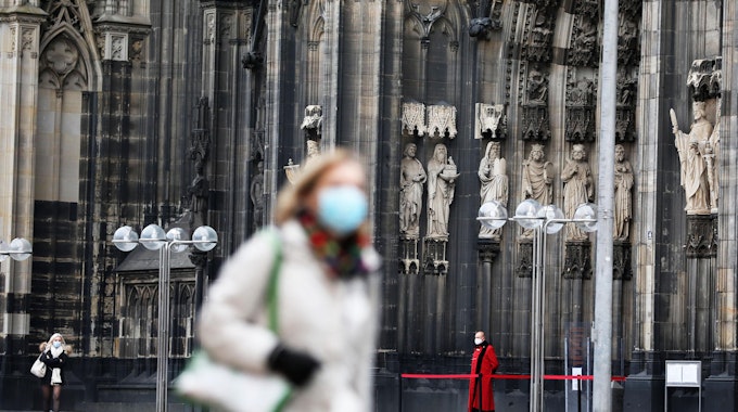 Eine Frau mit Corona-Maske vor dem Kölner Dom