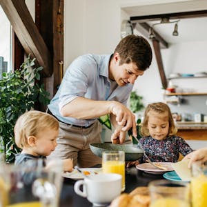 Eine Familie mit Vater, Mutter und zwei Kindern sitzt am Frühstückstisch