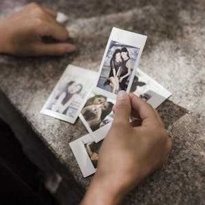 Eine Hand hält alte Polaroids, auf denen zwei Freundinnen zusammen sind.