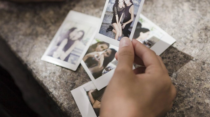 Eine Hand hält alte Polaroids, auf denen zwei Freundinnen zusammen sind.