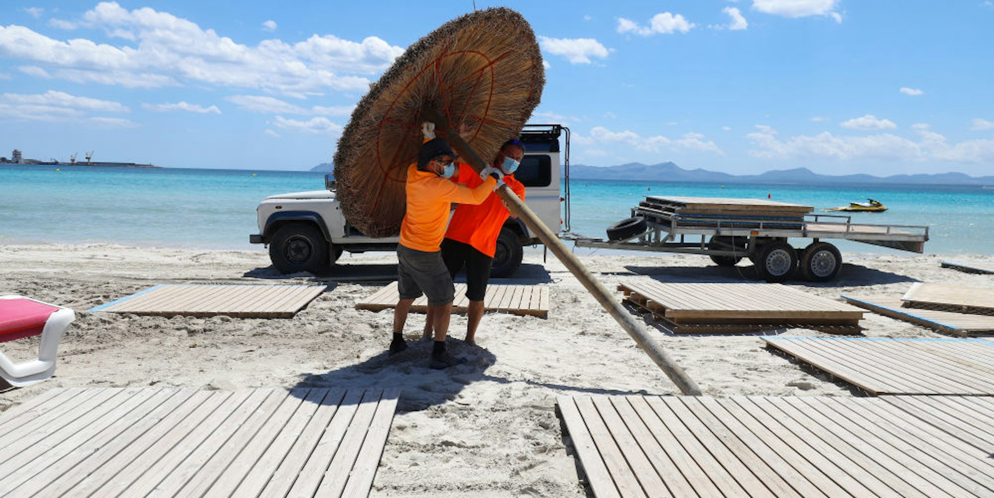 Vorbereitung auf die Urlauber: Männer mit Mundschutz stellen Sonnenschirme am Strand Alcudia auf.